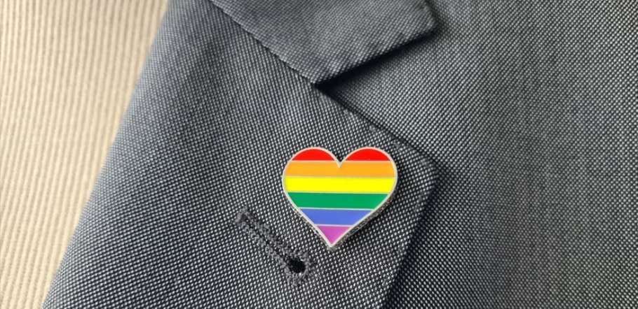a photo of a gray blazer lapel with a rainbow LGBTQ pin in the shape of a heart